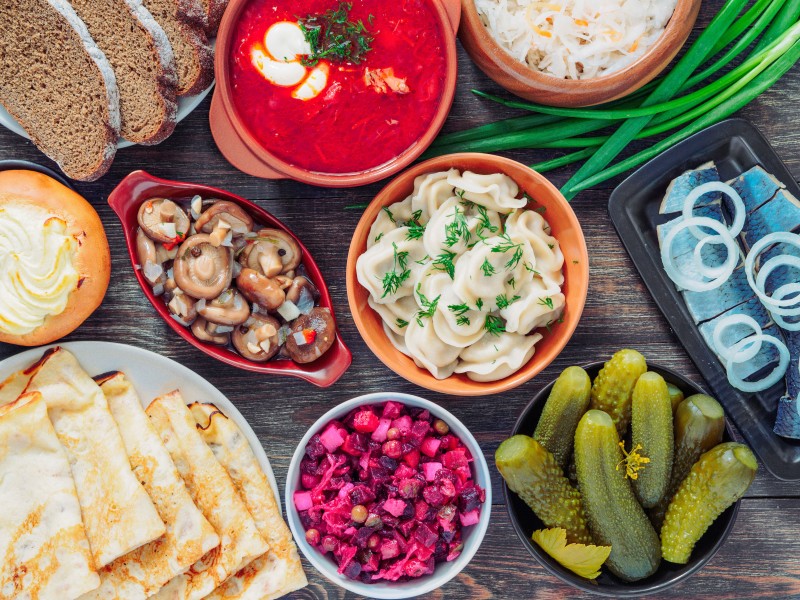 Wooden-table-with-dishes-of-russian-cuisine-borscht-pelmeni-herring-marinated-mushrooms-salted-cucumbers-vinaigrette-sauerkraut-rye-bread-pancakes-cheese-pastry-Russia-Global-Storybook-2